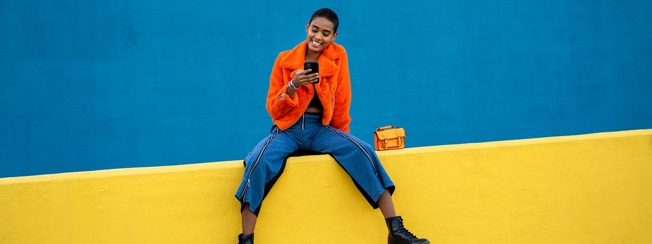 young woman sitting on colorful wall